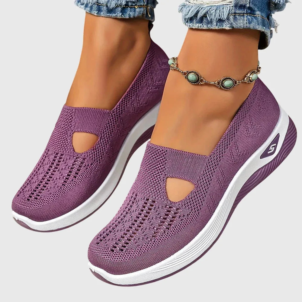 Purple knitted slip-on trainers shown from above resting in hand, revealing perforated sole