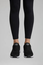 Front view of black knit trainers worn with black leggings, showing lace detail and heel tab