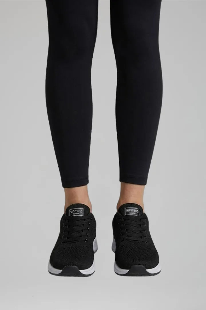 Front view of black knit trainers worn with black leggings, showing lace detail and heel tab