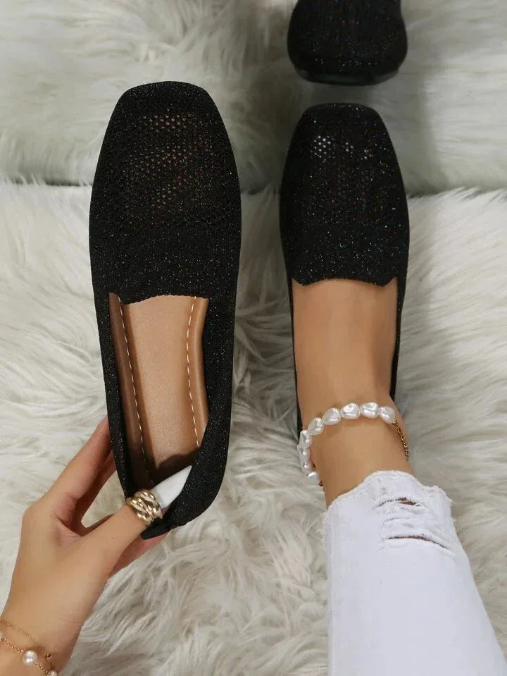 Black glitter-knit slip-on flats with mesh toe detail and tan insole, held by hand