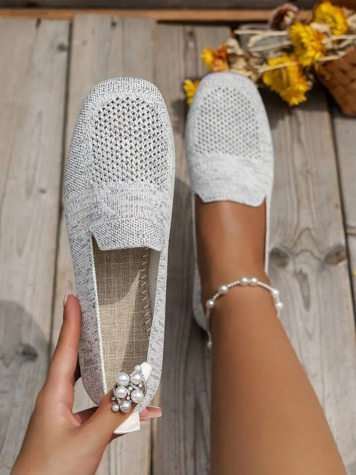 Grey knitted flats with woven straw-textured insole, shown side by side outdoors