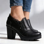 Close-up side profile of black leather ankle boot with lace trim, zip pull and stacked block heel