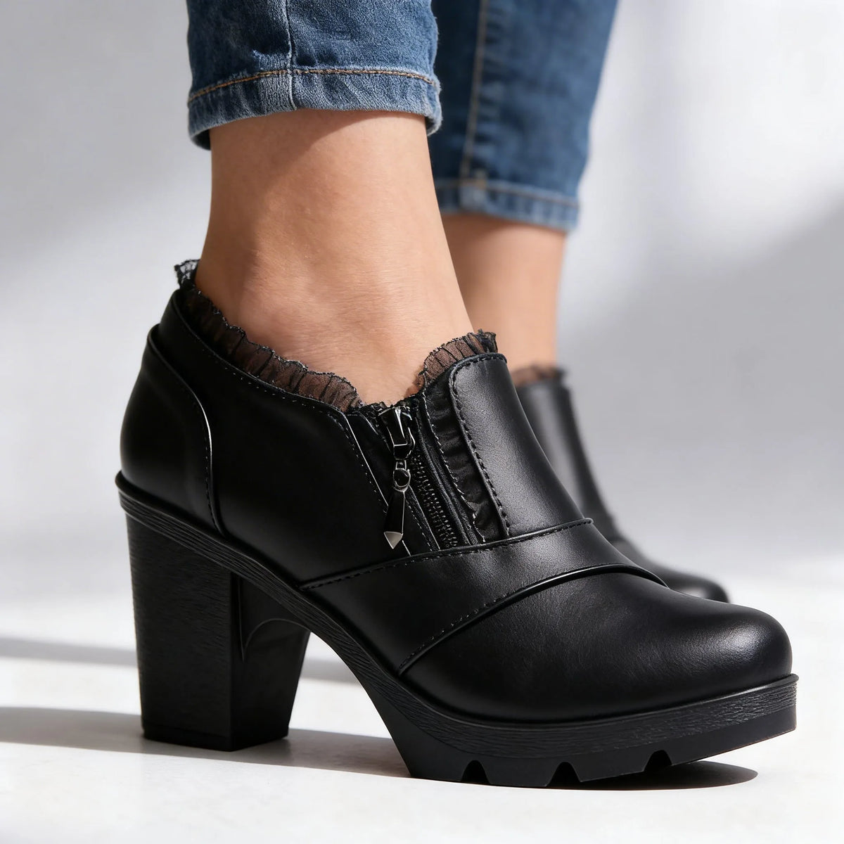Close-up side profile of black leather ankle boot with lace trim, zip pull and stacked block heel