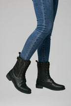 Side profile of black combat boots with buckle detail and lace-up front worn with skinny jeans
