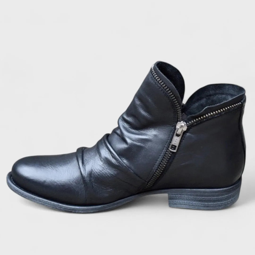 Black leather ankle boot shown in profile with ruched vamp and exposed metal side zip detail