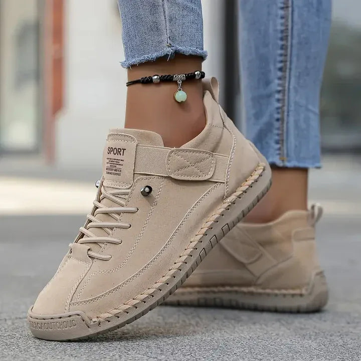 Beige suede-style trainer with adjustable strap and lace-up front, side profile on foot