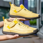 Pair of yellow leather trainers held by hand, showing stitched sole and hook-and-loop strap