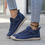 Navy blue suede-look trainer with tan sole and adjustable strap, worn with jeans