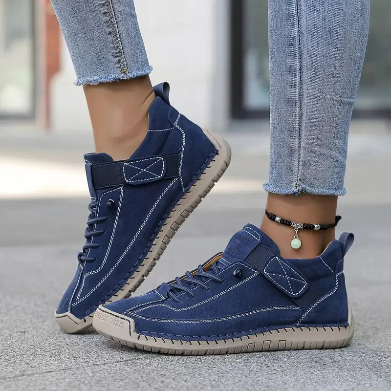 Navy blue suede-look trainer with tan sole and adjustable strap, worn with jeans