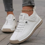 White leather trainer with tan sole, shown on foot styled with grey trousers