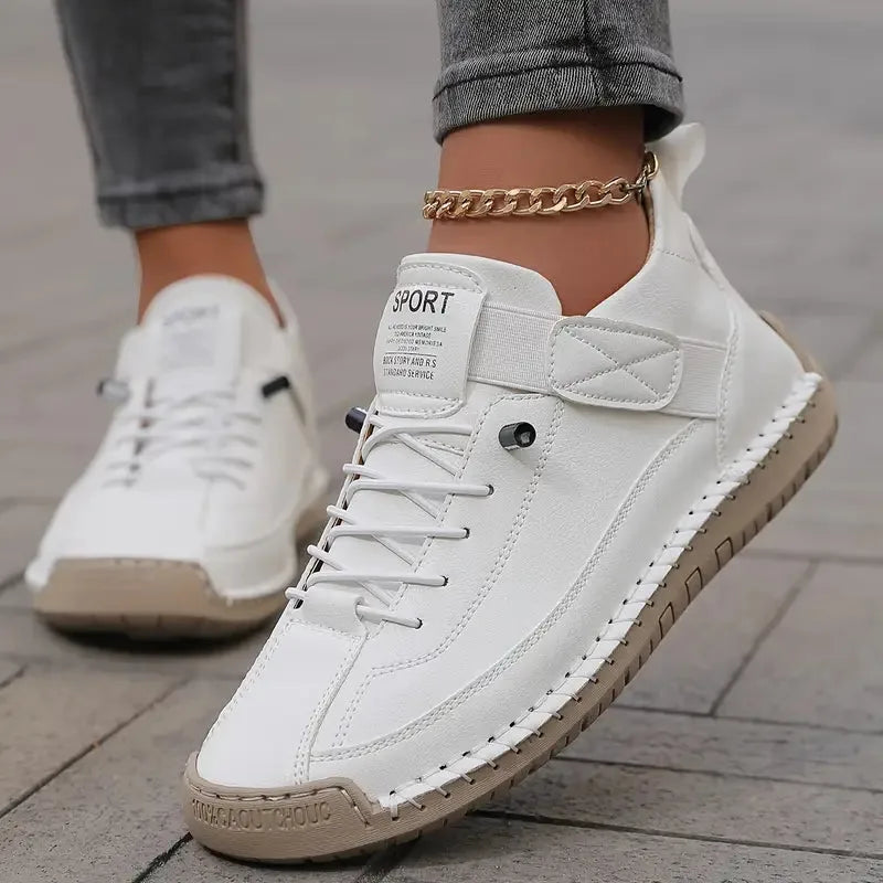 White leather trainer with tan sole, shown on foot styled with grey trousers