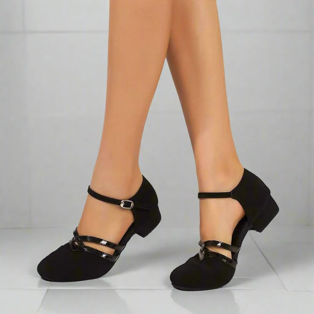 Side view of black suede low-heel dance shoes with patent ankle strap and buckle on model's feet
