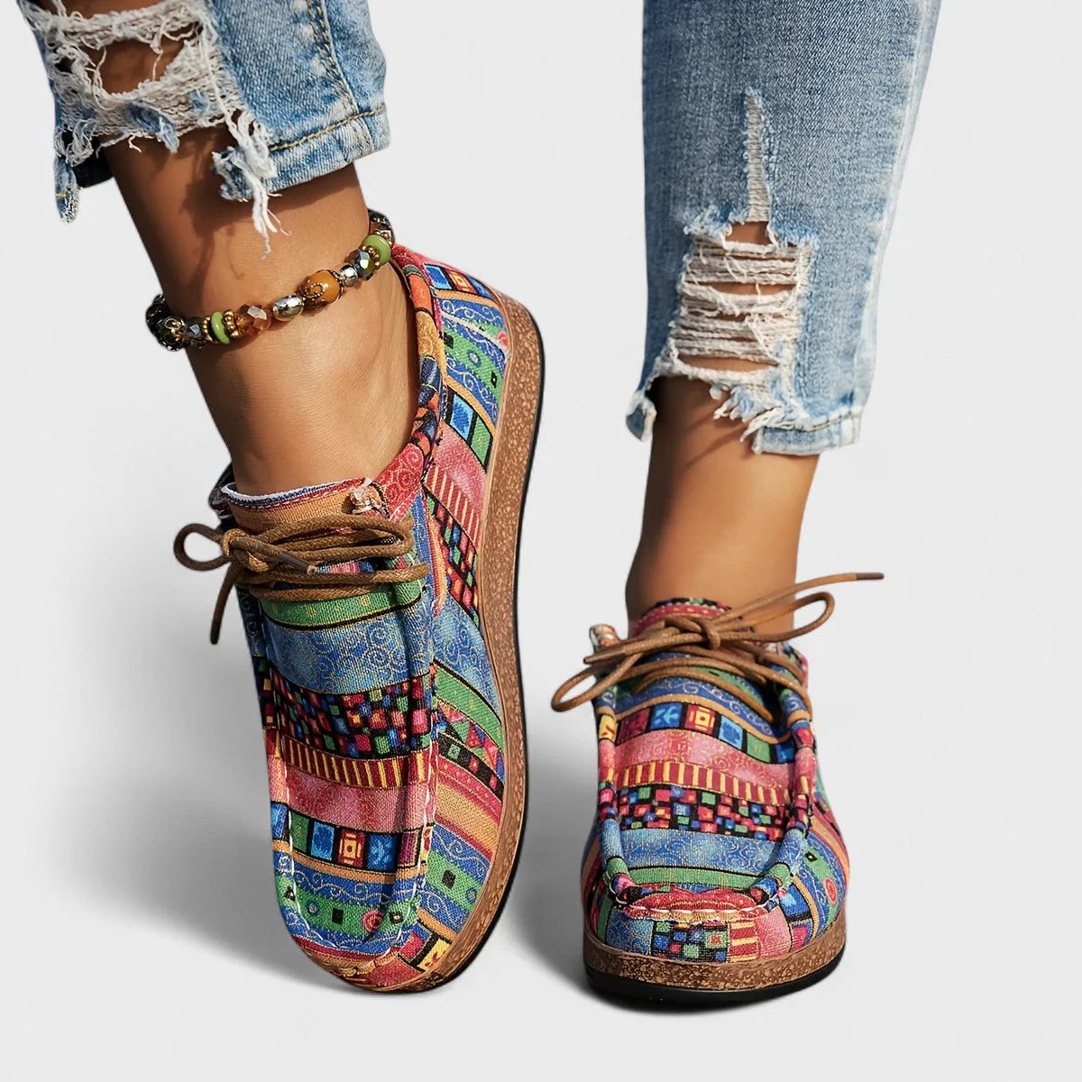Close-up back view of colourful pink, blue and green patchwork lace-up shoes with a beaded anklet.