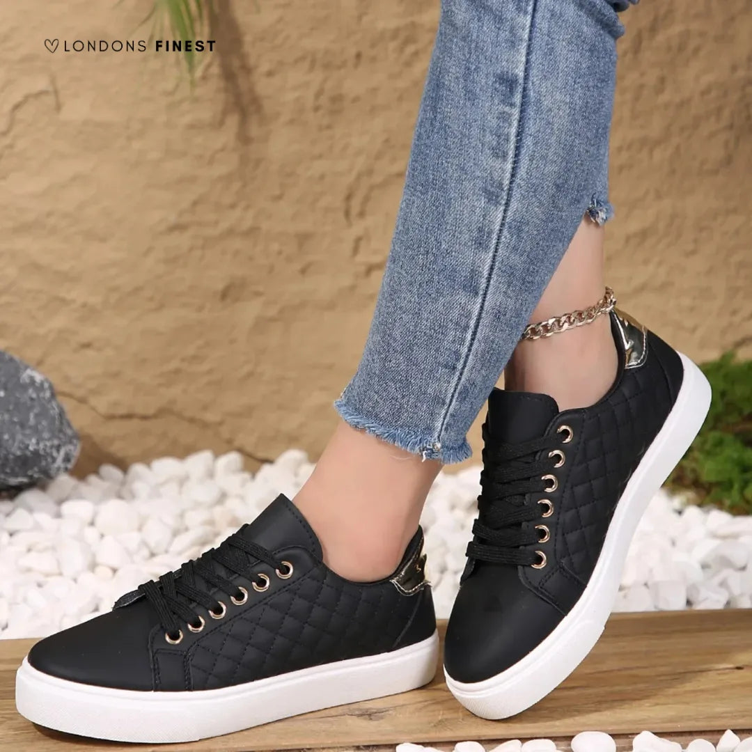 Black quilted lace-up trainers with white sole and metallic heel accent, styled with denim and a chain anklet.