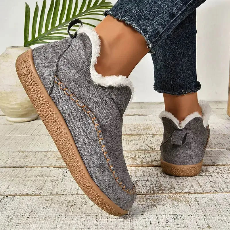 Side view of grey suede ankle boot with white faux fur trim and contrast stitching, worn with cropped jeans