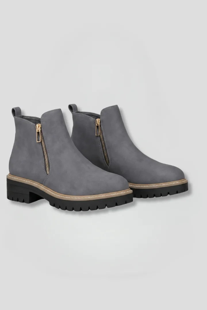 Front angled view of a pair of grey suede-effect ankle boots with gold-tone side zips and lug soles