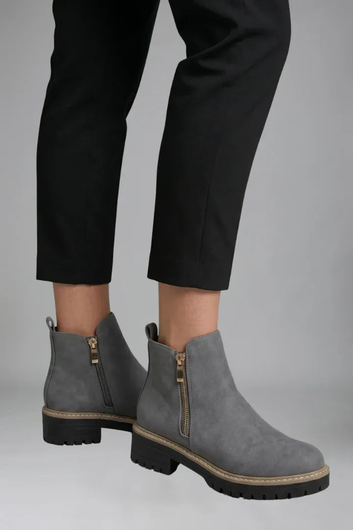 Angled side view of grey ankle boots worn with black trousers, showing the rounded toe and block heel