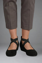 Close-up front view of feet in grey cropped trousers wearing black suede ballet flats with crisscross straps