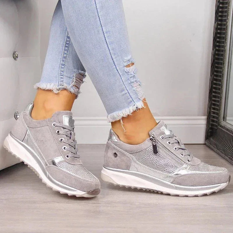Top view of grey suede trainers with silver accents and tan insole, paired with sunglasses and a watch