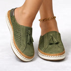 Green suede slip-on trainer shown from the side, with perforated panels, tassel detail and cork-style trim