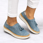 Dusty blue suede slip-on trainers on feet, close-up of tassel front and perforated side cut-outs