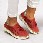 Red suede slip-on trainer worn with cropped white trousers, showing metallic heel accent and cushioned sole