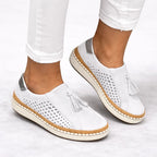 White suede slip-on trainers on feet, front angle highlighting tassel trim and breathable perforations