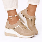 Side view of beige wedge trainers with gold metallic trim and perforated panels, worn with cream jeans