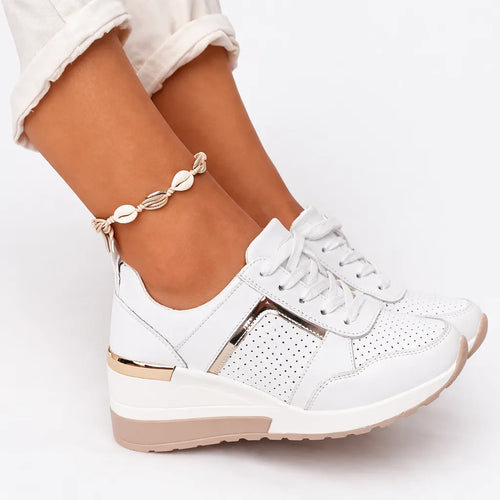 Close-up of white wedge trainers with gold zip-style panel and lace-up front, shown on foot