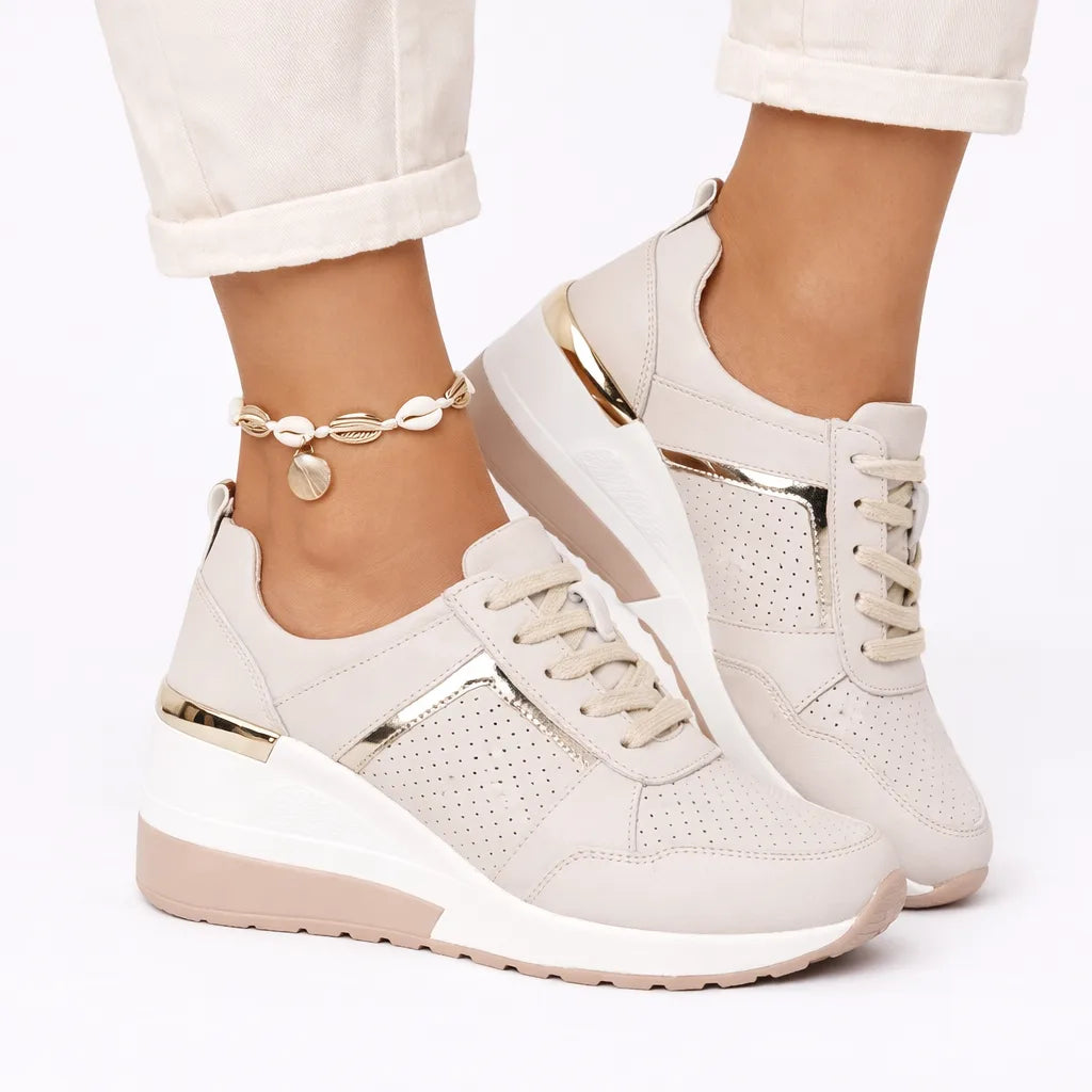 Front angle of beige wedge trainers with gold trim, perforated toe panel and lace-up fastening