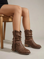 Model seated wearing brown mid-calf slouch boots with braided tassel wrap strap and stacked block heel