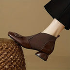 Close-up side view of a brown croc-embossed leather ankle boot with knit stretch panel and round buckle detail, worn on foot