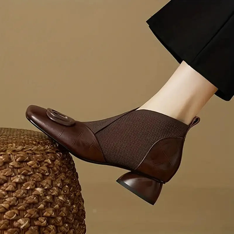 Close-up side view of a brown croc-embossed leather ankle boot with knit stretch panel and round buckle detail, worn on foot