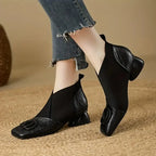 Front angled view of black stretch-knit ankle boots with croc-textured leather trim and sculpted block heel, paired with jeans