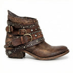 Side view of brown distressed leather ankle boot with layered buckle straps, studs and chain detail