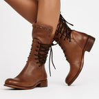 Side view of brown leather lace-up mid-calf boots worn on crossed legs, showing studded cuff detail
