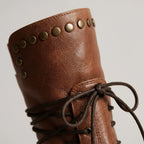 Close-up of the studded cuff and knotted lace tie on a brown leather boot