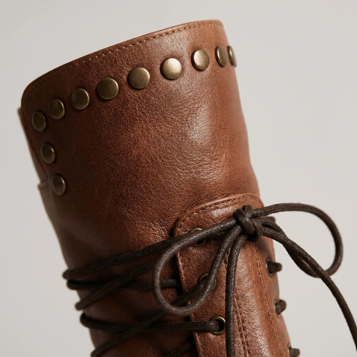 Close-up of the studded cuff and knotted lace tie on a brown leather boot