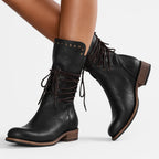Side view of black leather lace-up mid-calf boots worn on crossed legs, showing studded cuff trim
