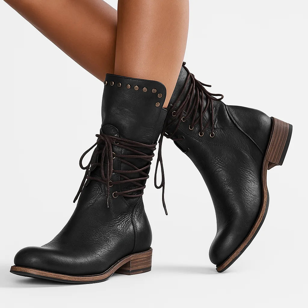 Side view of black leather lace-up mid-calf boots worn on crossed legs, showing studded cuff trim
