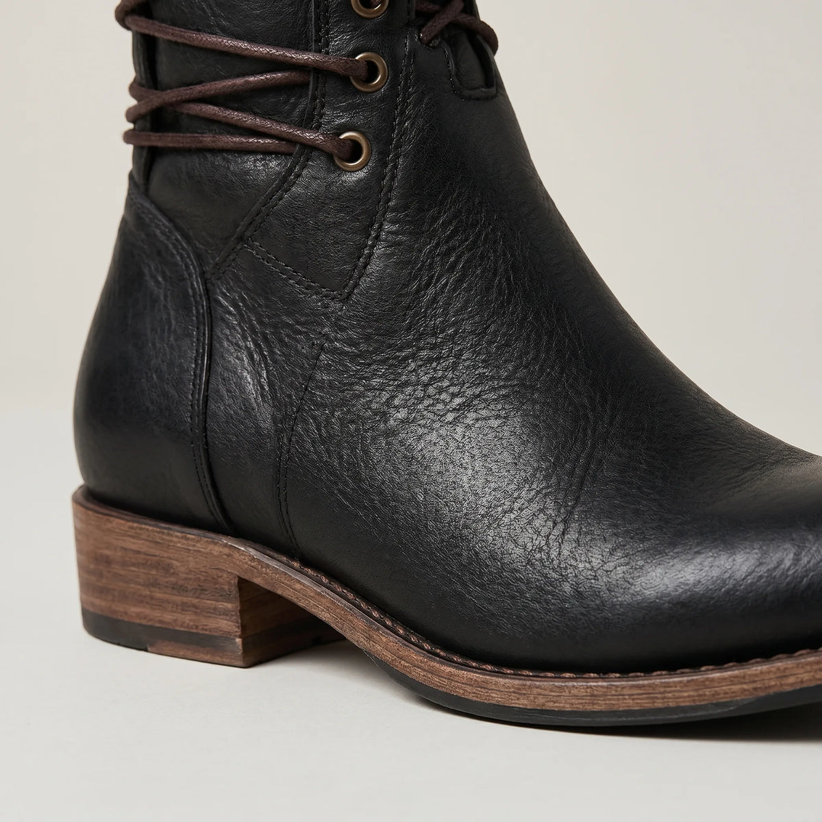 Close-up of the black leather boot's lacing eyelets and stacked wooden block heel