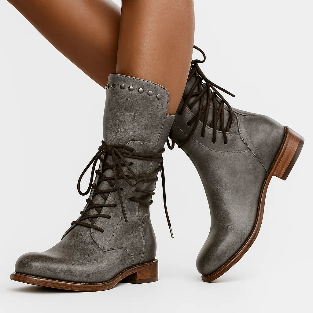 Side view of grey leather lace-up mid-calf boots worn on crossed legs, showing studded cuff and laces