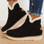 Side profile of black suede ankle boot with cream faux fur cuff, tan heel accent and stitched moccasin toe