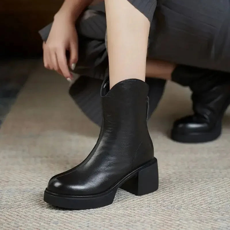 Black leather Chelsea boot on foot with elastic side panel, styled with a pleated grey skirt while crouching