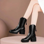 Pair of black leather ankle boots styled on a pink pedestal, showing rounded toe and chunky block heel