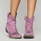 Pink suede cowboy ankle boots with pull tabs, pointed toe and low stacked heel, front view.