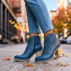 Blue leather western-style ankle boots with contrast stitching and wooden block heel, shown on model walking outdoors