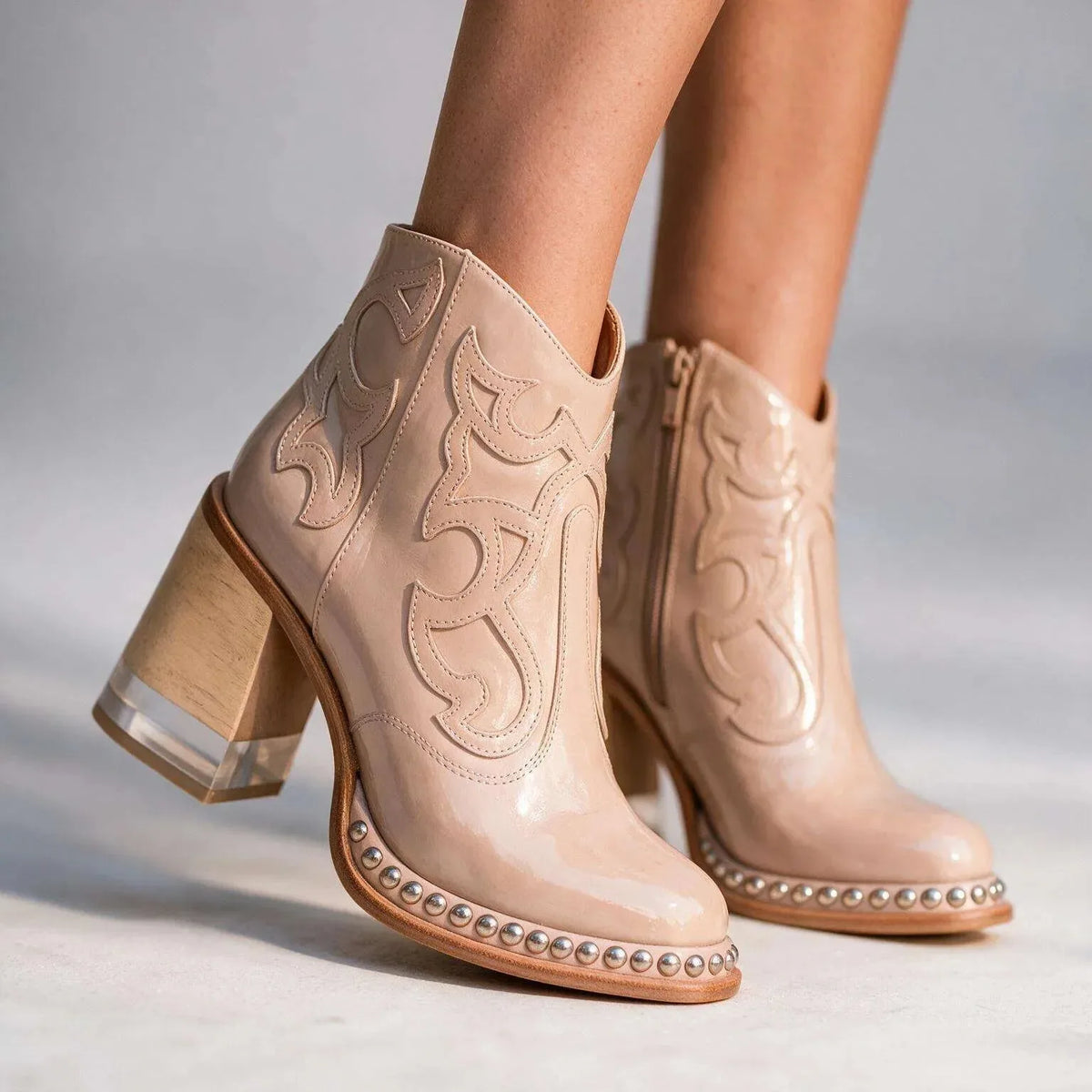 Nude patent leather western ankle boots with tonal embroidery stitching and studded sole trim