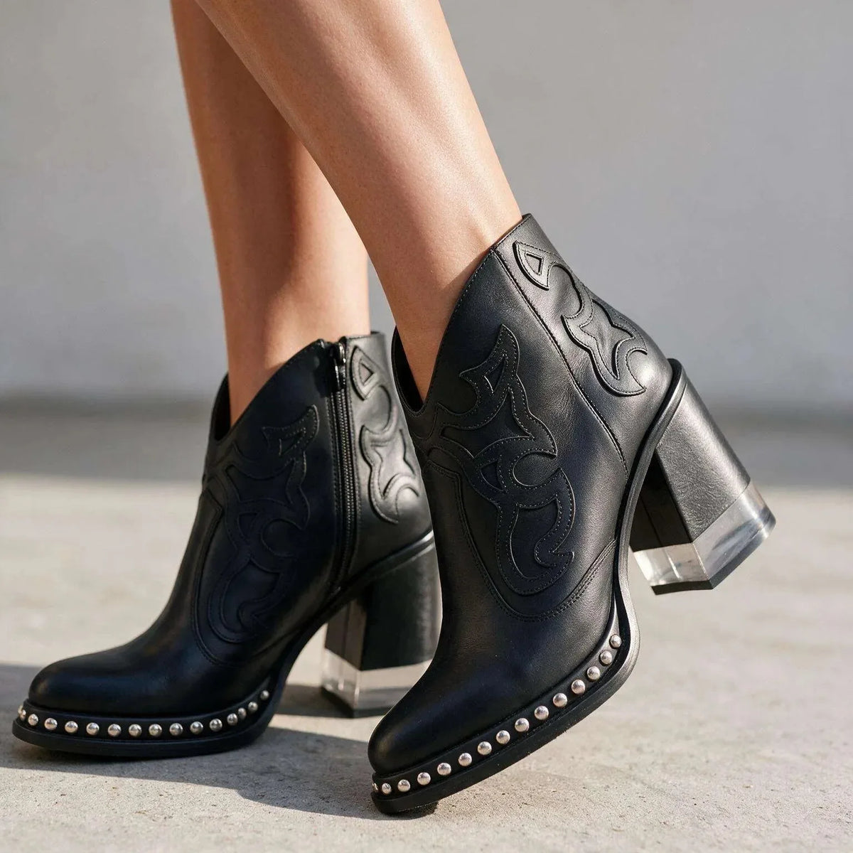 Black leather western ankle boots shown close up with clear block heel and studded outsole detail