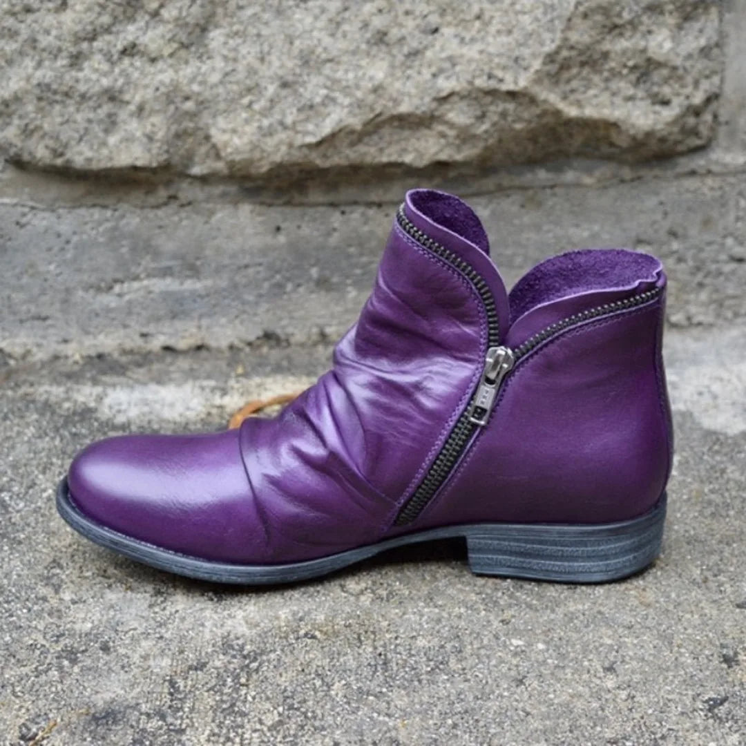 Side view of a purple leather ankle boot with slouchy ruching and a silver double zip detail.